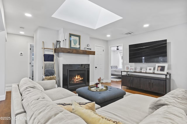 living area featuring a glass covered fireplace, a skylight, wood finished floors, and recessed lighting