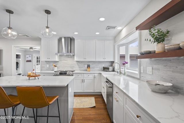 kitchen with white cabinets, stove, stainless steel dishwasher, wall chimney range hood, and a sink