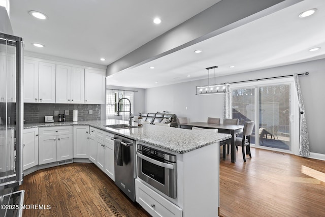 kitchen featuring a sink, a peninsula, stainless steel appliances, white cabinetry, and dark wood-style flooring