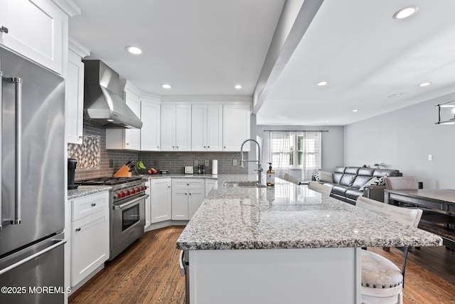 kitchen featuring dark wood-style floors, high quality appliances, a breakfast bar, a sink, and wall chimney exhaust hood