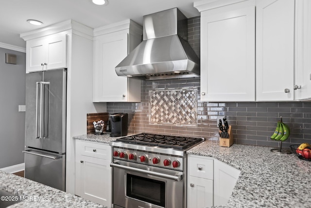 kitchen with backsplash, white cabinets, high end appliances, and wall chimney range hood