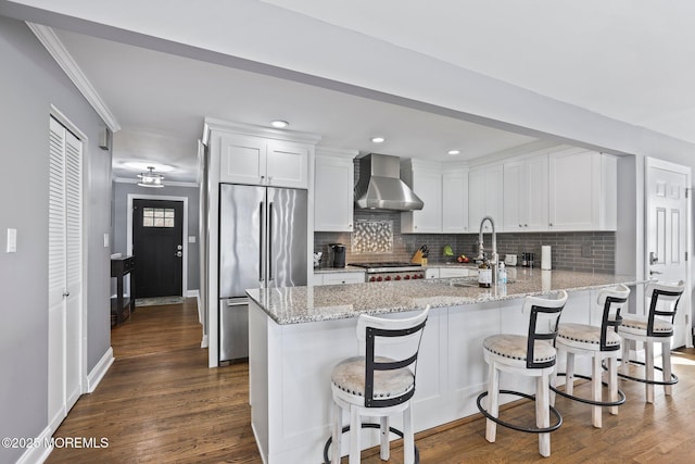 kitchen with high end fridge, dark wood-style floors, white cabinetry, a peninsula, and wall chimney exhaust hood