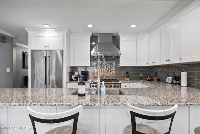 kitchen with light stone countertops, white cabinetry, high end fridge, and wall chimney range hood