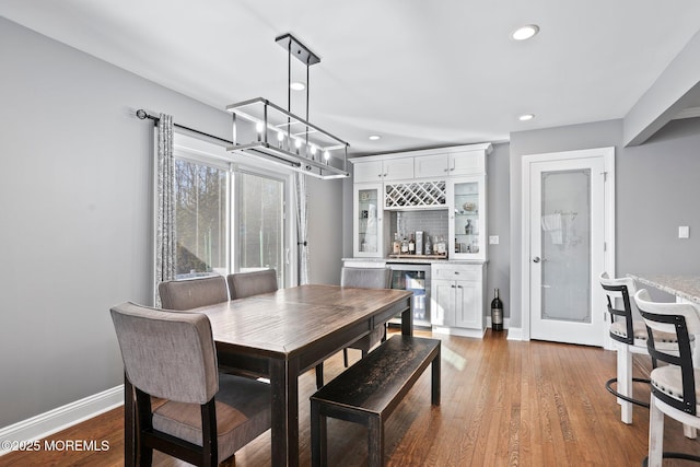 dining space featuring beverage cooler, a dry bar, wood finished floors, and baseboards