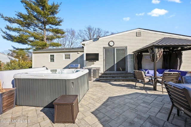 back of house with entry steps, a hot tub, a gazebo, outdoor lounge area, and a patio area