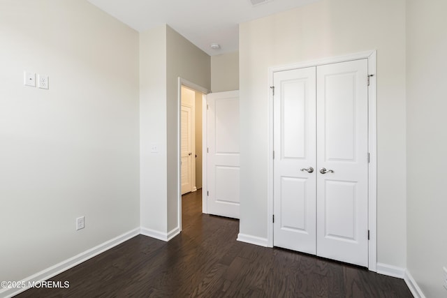 unfurnished bedroom featuring dark wood-style floors, visible vents, baseboards, and a closet