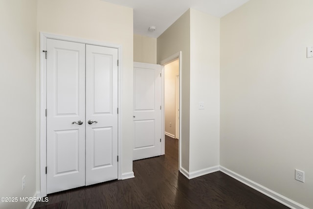 unfurnished bedroom with a closet, baseboards, and dark wood-type flooring