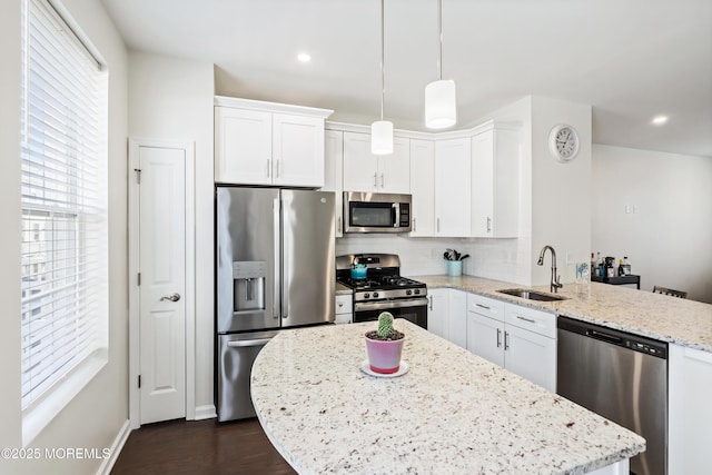 kitchen featuring hanging light fixtures, appliances with stainless steel finishes, white cabinets, a sink, and light stone countertops