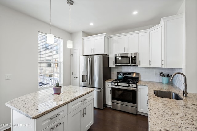 kitchen with white cabinets, light stone counters, stainless steel appliances, and a sink