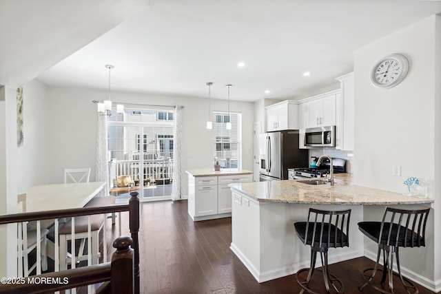 kitchen featuring pendant lighting, appliances with stainless steel finishes, white cabinetry, light stone countertops, and a peninsula