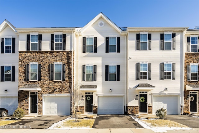 townhome / multi-family property with a garage, stone siding, and driveway