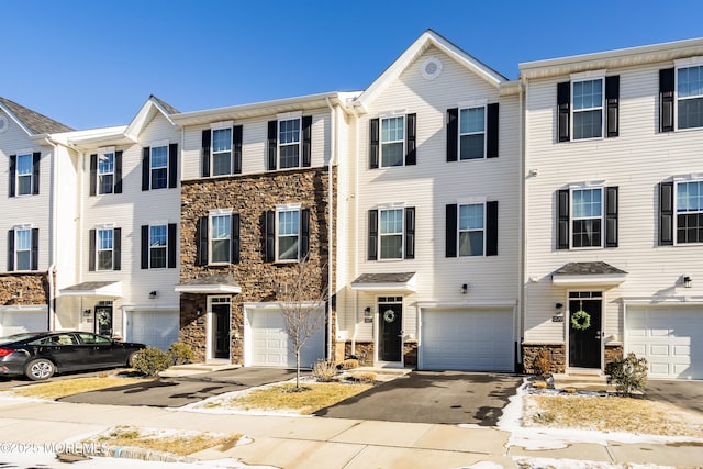 townhome / multi-family property with a garage, driveway, and stone siding