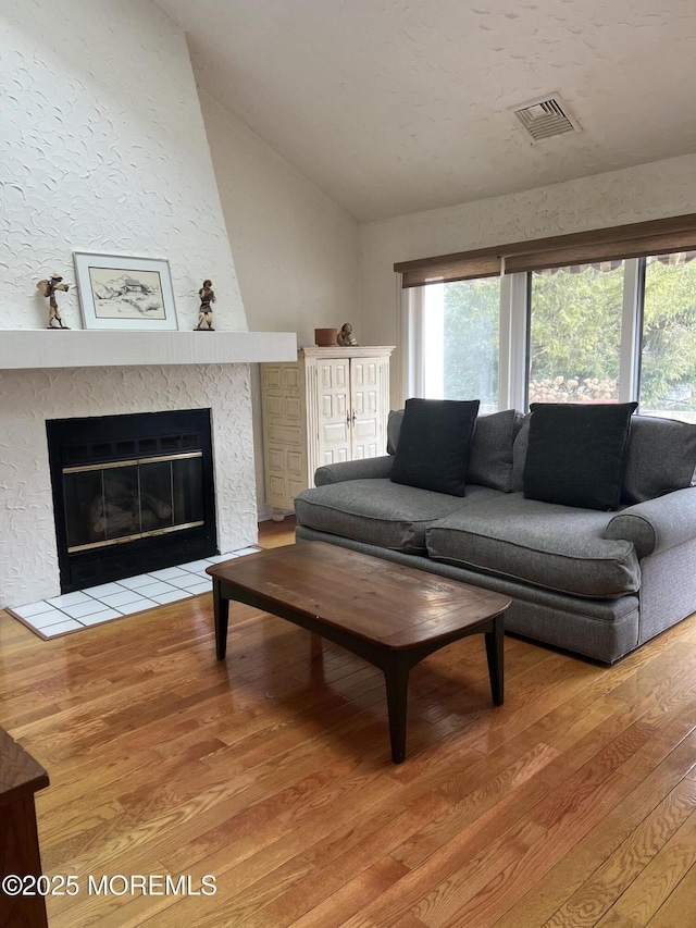 living room featuring lofted ceiling, visible vents, a large fireplace, wood finished floors, and plenty of natural light