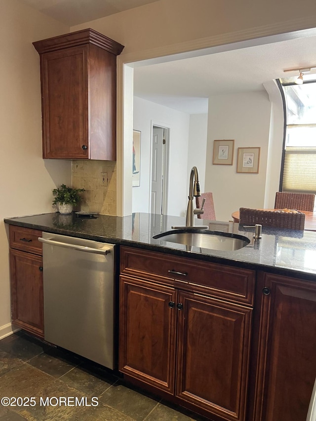 kitchen featuring a sink, stainless steel dishwasher, tasteful backsplash, dark stone countertops, and stone tile flooring