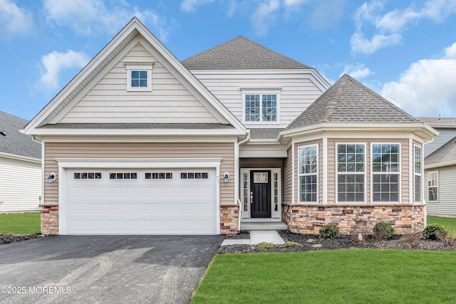 view of front of house with driveway, stone siding, a garage, and roof with shingles