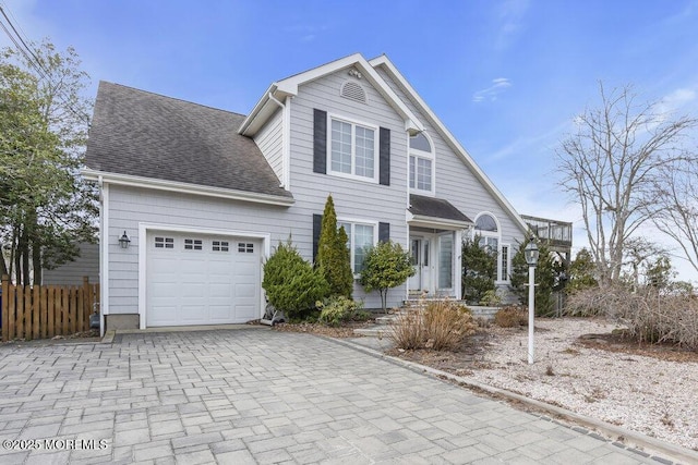 traditional home featuring a garage, a shingled roof, fence, and decorative driveway