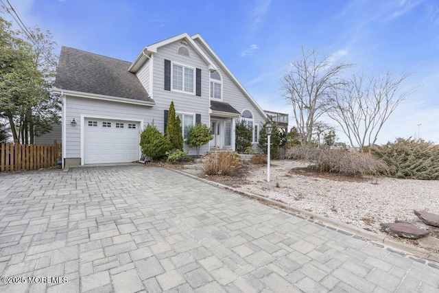 view of front facade featuring a garage, roof with shingles, decorative driveway, and fence