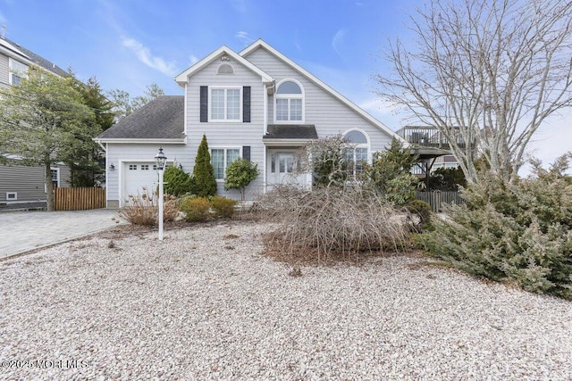 traditional-style house featuring a garage, a shingled roof, decorative driveway, and fence