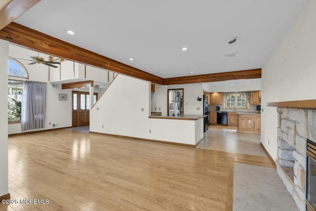 unfurnished living room featuring light wood-style floors, beam ceiling, a fireplace, and baseboards