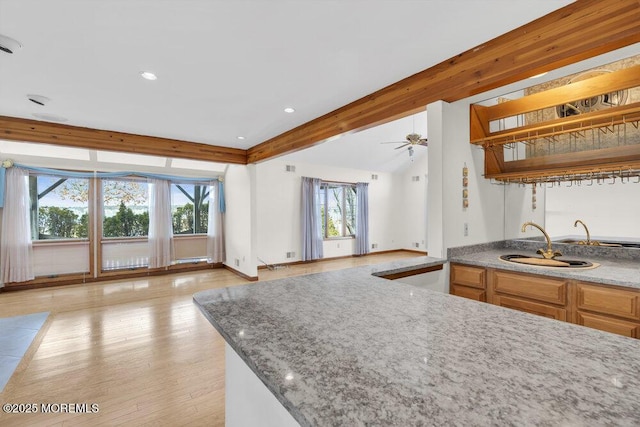 kitchen with lofted ceiling with beams, stone countertops, open floor plan, a sink, and light wood-type flooring