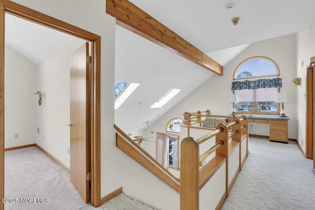 hallway with light carpet, beamed ceiling, a skylight, and an upstairs landing