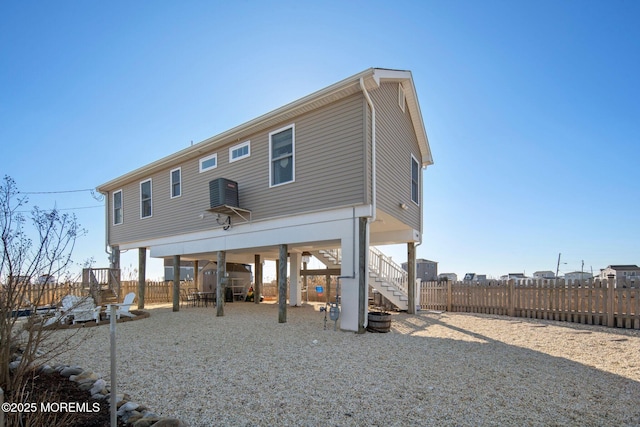 rear view of property featuring a carport, stairway, cooling unit, and fence