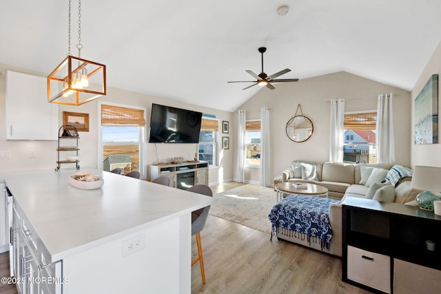 living room featuring vaulted ceiling, ceiling fan with notable chandelier, plenty of natural light, and light wood-style flooring