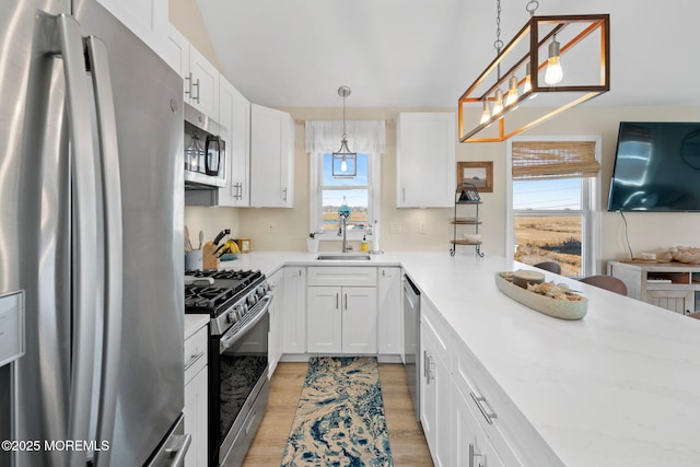 kitchen featuring stainless steel appliances, a sink, decorative light fixtures, and white cabinets