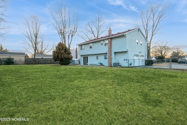 rear view of house featuring a garage, central AC, fence, a lawn, and a chimney