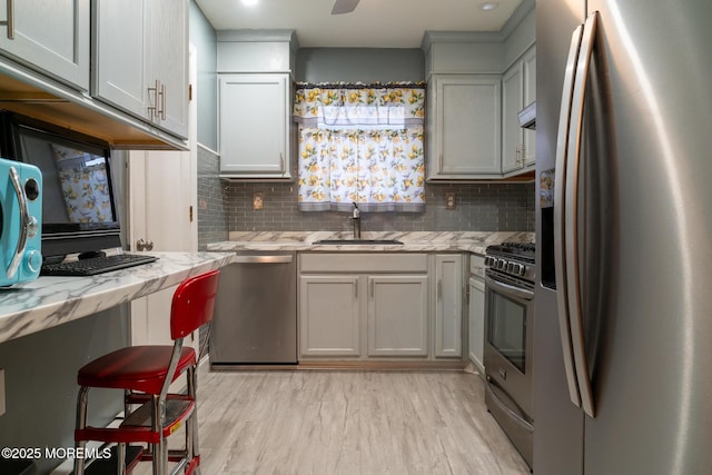 kitchen with light stone counters, backsplash, appliances with stainless steel finishes, light wood-style floors, and a sink