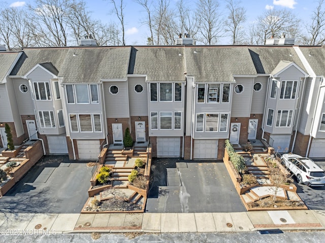 multi unit property with driveway, an attached garage, a shingled roof, and brick siding