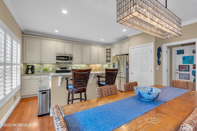 kitchen with stainless steel appliances, a kitchen island, a kitchen breakfast bar, ornamental molding, and glass insert cabinets