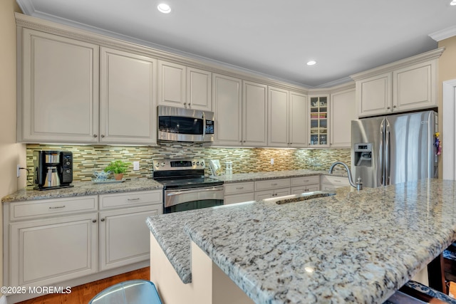 kitchen featuring a sink, appliances with stainless steel finishes, light stone countertops, a kitchen bar, and glass insert cabinets