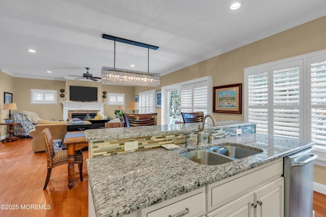 kitchen with a fireplace, a sink, white cabinets, hanging light fixtures, and crown molding