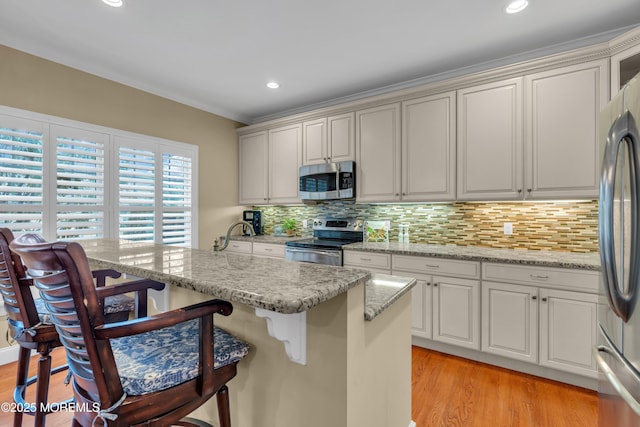 kitchen featuring appliances with stainless steel finishes, light stone countertops, a breakfast bar, and light wood-style floors