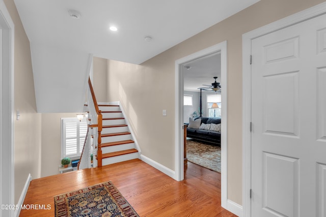 stairway with wood finished floors, a ceiling fan, and baseboards