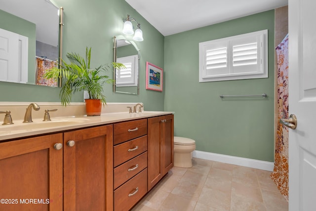 bathroom with toilet, a sink, baseboards, and double vanity