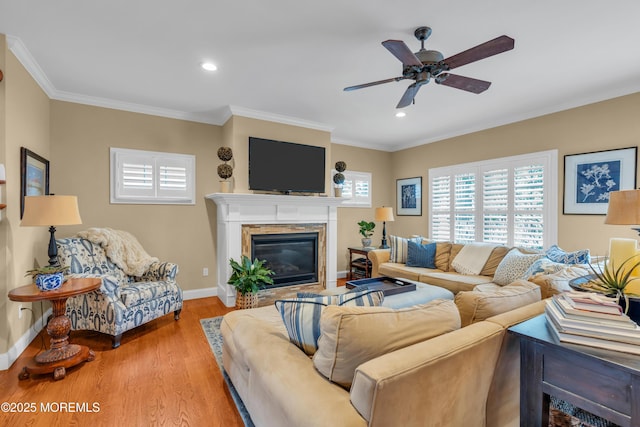 living room featuring a ceiling fan, baseboards, ornamental molding, light wood finished floors, and a glass covered fireplace