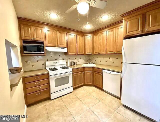 kitchen featuring light tile patterned floors, under cabinet range hood, white appliances, a sink, and light countertops