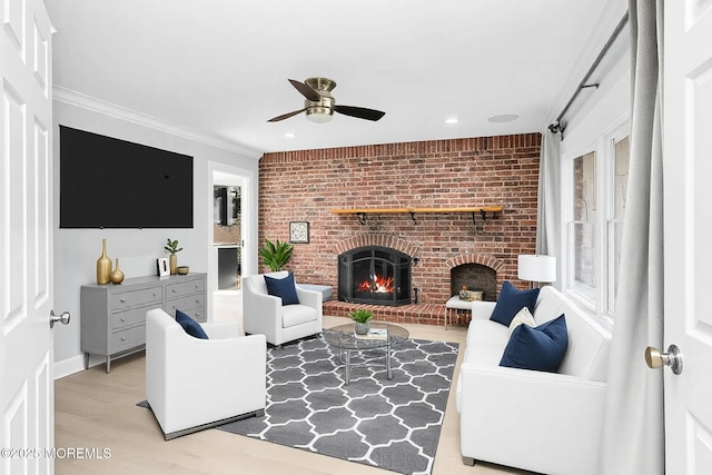 living area with light wood-style floors, ceiling fan, a fireplace, and crown molding