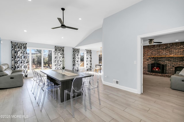 dining room with a brick fireplace, visible vents, light wood-style floors, and a ceiling fan