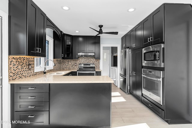 kitchen with appliances with stainless steel finishes, dark cabinetry, a sink, and glass insert cabinets