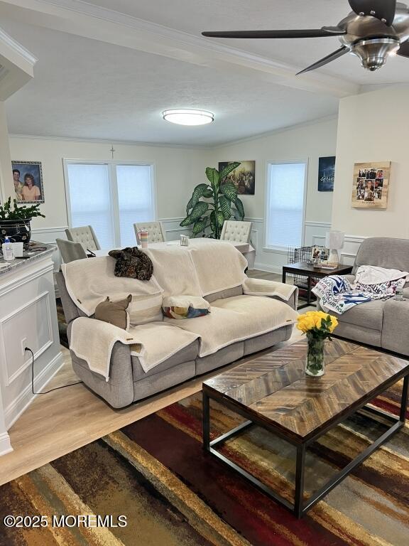 living area with a wainscoted wall, lofted ceiling, a decorative wall, ceiling fan, and light wood-type flooring