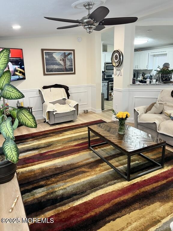 living room with a decorative wall, wood finished floors, a ceiling fan, vaulted ceiling, and wainscoting