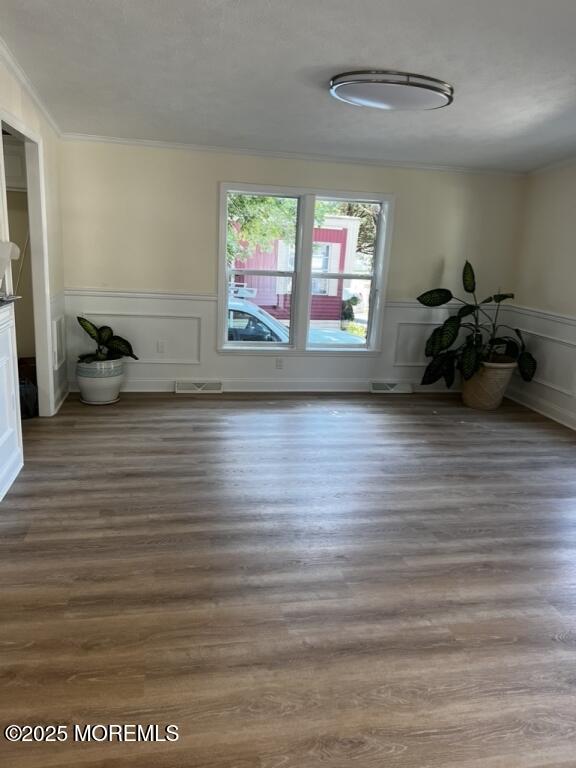 empty room featuring dark wood-style floors, ornamental molding, and wainscoting