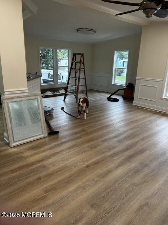 recreation room featuring wainscoting, ceiling fan, a decorative wall, and wood finished floors