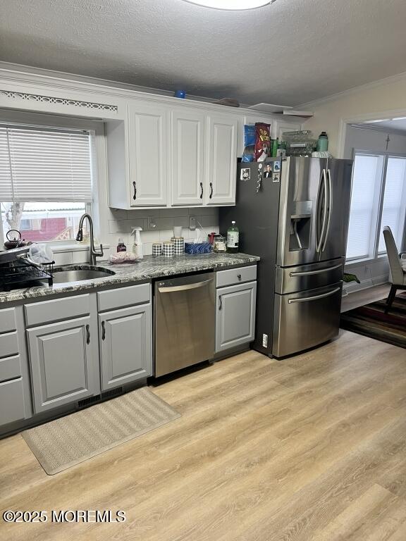 kitchen featuring stainless steel appliances, ornamental molding, light wood-type flooring, and a sink