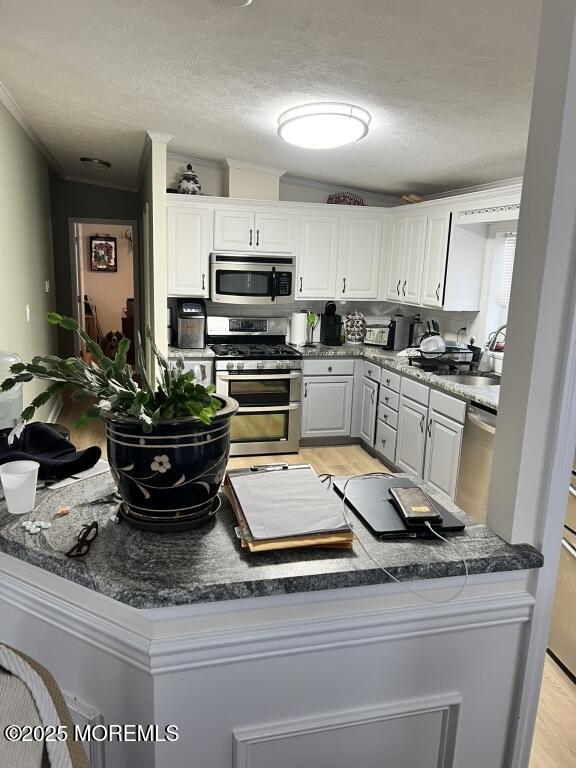 kitchen with stainless steel appliances, dark countertops, white cabinets, and a textured ceiling