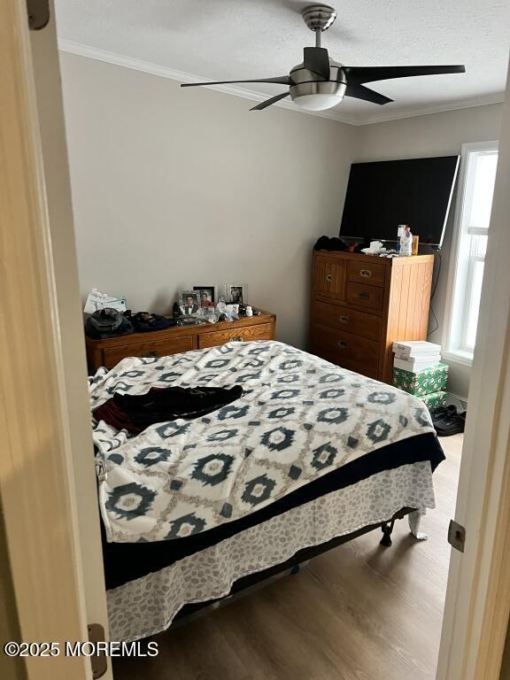 bedroom with ceiling fan, ornamental molding, a textured ceiling, and wood finished floors