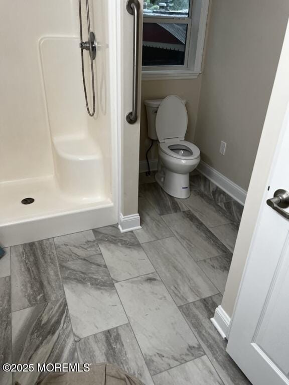 bathroom featuring toilet, a stall shower, baseboards, and marble finish floor